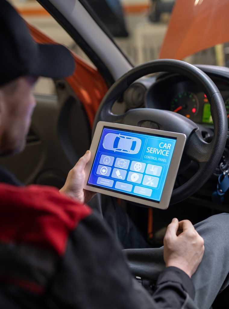 Young repairman with digital tablet sitting in front of steer and looking at icons and options on home page of car service website on screen